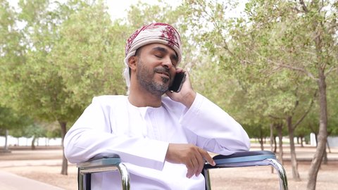 الاطمئنان على الاهل والاصدقاء عبر الجوال، التجول والتنزه فى الهواء الطلق، توفير اجهزة ومعدات تساعد بالحركة والتنقل ، العنايه بأصحاب الهمم وتأمين احتياجاتهم الخاصة، تصوير لشاب عربي خليجي عماني مقعد يرتدي الكمه و الدشداشة يجلس على كرسي متحرك