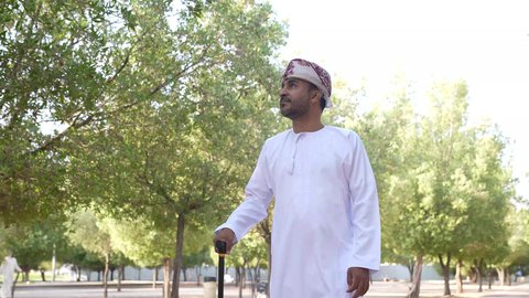 الاستمتاع بالأجواء في إحدى المنتزهات ، التجول والتنزه فى الهواء الطلق ، مفهوم الاستجمام بالطبيعة ، رجل عربي خليجي عماني يستند على عكاز ، يرتدي الزي العماني يسير فى احدي حدائق سلطنة عمان، الخروج إلى أحد الاماكن العامة للترفيه عن النفس