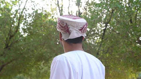 الاستمتاع بالأجواء في إحدى المنتزهات ، التجول والتنزه فى الهواء الطلق ، مفهوم الاستجمام بالطبيعة ، رجل عربي خليجي عماني يرتدي الزي العماني يسير فى احدي حدائق سلطنة عمان، الخروج إلى أحد الاماكن العامة للترفيه عن النفس