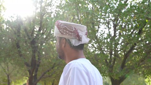 التجول والتنزه فى الهواء الطلق ، مفهوم الاستجمام بالطبيعة ، الاستمتاع بالأجواء في إحدى المنتزهات ،رجل عربي خليجي عماني يرتدي الزي العماني يسير فى احدي حدائق سلطنة عمان، الخروج إلى أحد الاماكن العامة للترفيه عن النفس
