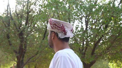 الاستمتاع بالأجواء في إحدى المنتزهات ،رجل عربي خليجي عماني يرتدي الزي العماني يسير فى احدي حدائق سلطنة عمان، الخروج إلى أحد الاماكن العامة للترفيه عن النفس، التجول والتنزه فى الهواء الطلق ، مفهوم الاستجمام بالطبيعة