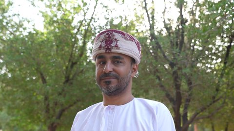 رجل عربي خليجي عماني يرتدي الزي العماني يسير فى احدي حدائق سلطنة عمان، الخروج إلى أحد الاماكن العامة للترفيه عن النفس، التجول والتنزه فى الهواء الطلق ، مفهوم الاستجمام بالطبيعة ، الاستمتاع بالأجواء في إحدى المنتزهات