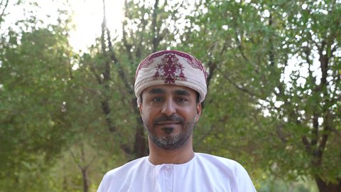 الخروج إلى أحد الاماكن العامة للترفيه عن النفس، التجول والتنزه فى الهواء الطلق ، مفهوم الاستجمام بالطبيعة ، الاستمتاع بالأجواء في إحدى المنتزهات، رجل عربي خليجي عماني يرتدي الزي العماني يسير فى احدي حدائق سلطنة عمان