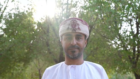 التجول والتنزه فى الهواء الطلق ، مفهوم الاستجمام بالطبيعة ، الاستمتاع بالأجواء في إحدى المنتزهات، الخروج إلى أحد الاماكن العامة للترفيه عن النفس، رجل عربي خليجي عماني يرتدي الزي العماني يسير فى احدي حدائق سلطنة عمان