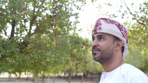 الاستمتاع بالأجواء في إحدى المنتزهات، الخروج إلى أحد الاماكن العامة للترفيه عن النفس، رجل عربي خليجي عماني يرتدي الزي العماني يسير فى احدي حدائق سلطنة عمان ، الاستجمام بالطبيعة واستنشاق الهواء الطلق