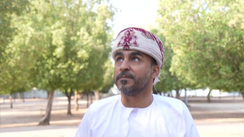 Going out to a public place to entertain yourself, an Arab Gulf Omani man wearing Omani clothing walking in one of the parks of the Sultanate of Oman, enjoying the atmosphere in one of the parks, relaxing in nature and breathing the fresh air