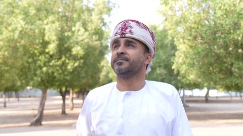 رجل عربي خليجي عماني يرتدي الزي العماني يسير فى احدي حدائق سلطنة عمان ، الاستمتاع بالأجواء في إحدى المنتزهات، الخروج إلى أحد الاماكن العامة للترفيه عن النفس،  الاستجمام بالطبيعة واستنشاق الهواء الطلق