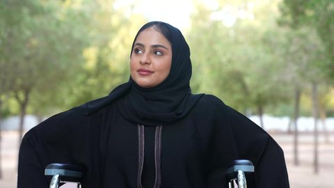 Providing devices and equipment that help with movement and mobility, caring for people with disabilities and ensuring their special needs, photographing a sick Omani Arab Gulf woman wearing a hijab and abaya sitting in a wheelchair, the disabled feeling of belonging, appreciation and respect in the Sultanate of Oman, enjoying the atmosphere in a park, relaxing in nature and breathing the fresh air.