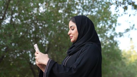 دمج التكنولوجيا الحديثه فى الحياه اليوميه ، الاستجمام بالطبيعة واستنشاق الهواء الطلق، تصوير من الخلف لسيدة عربية خليجية عمانية ترتدي الزي العماني تسير فى احدي حدائق سلطنة عمان ، اجراء المكالمات الهاتفية  ،شابه سعوديه تخرج إلى أحد الاماكن العامة للترفيه عن النفس