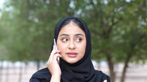 تصوير من الخلف لسيدة عربية خليجية عمانية ترتدي الزي العماني تسير فى احدي حدائق سلطنة عمان ، الاستجمام بالطبيعة واستنشاق الهواء الطلق، دمج التكنولوجيا الحديثه فى الحياه اليوميه  ، اجراء المكالمات الهاتفية  ،شابه سعوديه تخرج إلى أحد الاماكن العامة للترفيه عن النفس