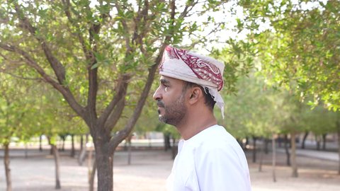 الاستجمام بالطبيعة واستنشاق الهواء الطلق، الاستمتاع بالأجواء في إحدى المنتزهات، تصوير لرجل عربي خليجي عماني يرتدي الزي العماني يسير فى احدي حدائق سلطنة عمان ،الخروج إلى أحد الاماكن العامة للترفيه عن النفس