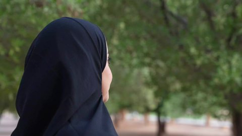A photograph from the back of an Omani Gulf Arab woman wearing Omani clothing walking in one of the parks in the Sultanate of Oman. Recreation in nature and fresh air, enjoying the atmosphere in a park. A young Saudi woman goes out to a public place for entertainment.