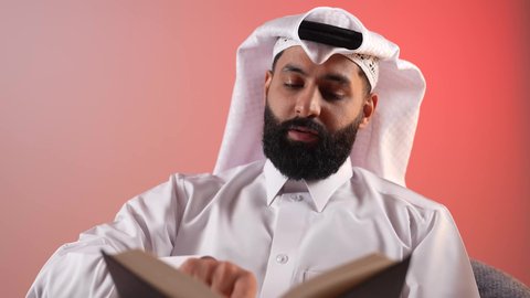 Increasing intellectual reserve, a young Saudi man reading books, stories and novels, developing skills and expanding knowledge and ideas, a close-up portrait of a Qatari Gulf Arab man wearing traditional thobe and ghutra sitting behind an office table holding a book in his hands, spending free time usefully, colorful background