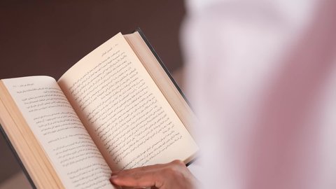 قضاء أوقات الفراغ بشكل مفيد، زيادة الذخيرة الفكرية، شاب سعودي يقوم بقراءة الكتب والقصص والروايات، تنمية المهارات وتوسيع المعارف والأفكار، بورتريه مقرب من الخلف لرجل عربي خليجي قطري يرتدي الثوب التقليدي والغترة يجلس خلف طاولة المكتب ويمسك بيديه كتاب، خلفية ملونة