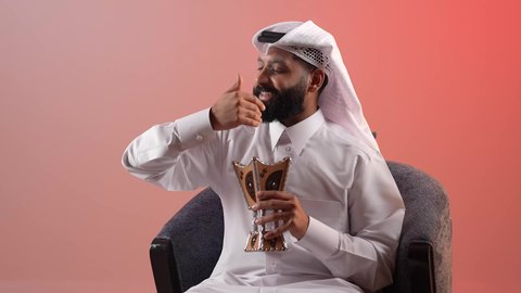 استخدام خشب العود  في الأعياد والمناسبات السعيدة، اتباع العادات والتقاليد العربية الأصيلة، شاب سعودي يقوم بالتبخير واستعمال العطور والمطيبات، بورتريه لرجل عربي خليجي قطري يرتدي الثوب التقليدي والغترة يجلس على كرسي ويمسك بيده المبخرة بايماءات الفرح، خلفية ملونة