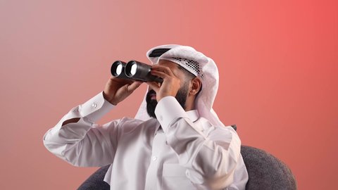 توضيح الرؤية وتقريبها، شاب سعودي يقوم باستخدام المنظار ثنائي العينين لمشاهدة الأشياء البعيدة، التخطيط ووضع الأهداف المستقبلية، بورتريه لرجل عربي خليجي قطري يرتدي الثوب التقليدي والغترة يجلس على كرسي ويضع تلسكوب ذو العدسات المقربة على عينيه، خلفية ملونة