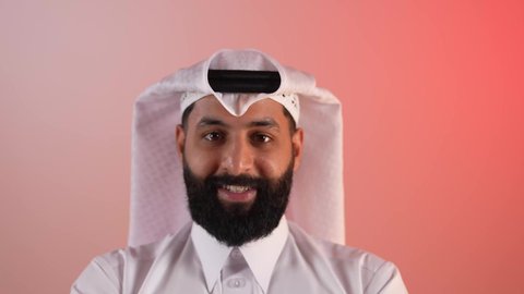 الاهتمام بالأناقة والمظهر الخارجي، شاب سعودي ينظر إلى الكاميرا بايماءات الجدية والسرور، مفهوم الرجولة والقوة والثقة بالنفس، بورتريه لرجل عربي خليجي قطري يرتدي الثوب التقليدي والغترة يقف بأيدي متقاطعة بتعابير الحزم، خلفية ملونة