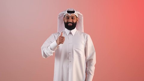التعبير عن الإعجاب والتقدير،شاب سعودي يرفع اصبع الإبهام للأعلى بعلامات الجودة والقبول، الشعور بالرضا والاستحسان،  الامتياز والعلامة الكاملة، بورتريه لرجل عربي خليجي قطري مبتسم يرتدي الثوب التقليدي والغتره ينظر للكاميرا بإيماءات السعادة، خلفية ملونة
