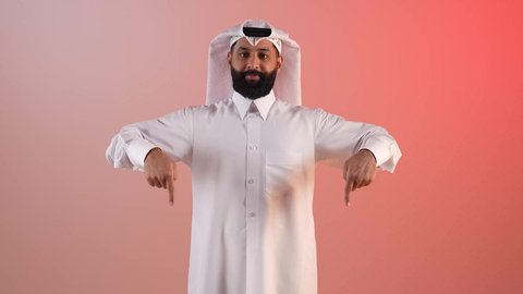تأكيد حدوث شيء هذه اللحظة, حركات تدل على هذا المكان (هنا)، شاب سعودي يقوم بتحديد موقع معين، بورتريه لرجل عربي خليجي قطري يرتدي الثوب التقليدي والغترة يشير بإصابع السبابة نحو الأسفل, النظر إلى الكاميرا بايماءات السرور، خلفية ملونة