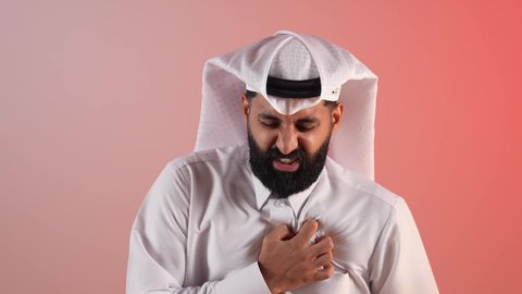 الذبحه الصدريه حالة مرضية، رجل سعودي ملتحي يظهر عليه التعب والإرهاق والضغوطات النفسية، بورتريه لشاب عربي خليجي قطري يرتدي الغترة و الثوب التقليدي يضع يده على قلبه يشعر بحالة سيئة من الوخز والألم في قلبه, خلفية ملونة
