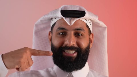 Locating something, Saudi young man pointing at someone, close-up portrait of a smiling Qatari Gulf Arab man wearing traditional thobe and ghutra pointing his index finger to the side, concept of elegance and concern for one's outward appearance, colorful background