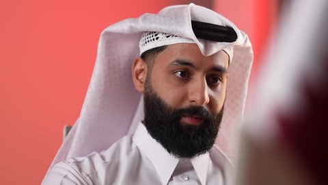 Merging business with technology and modern and advanced technology, a young Saudi man completing work via laptop, close-up portrait of a Qatari Gulf Arab man wearing traditional thobe and ghutra talking and conducting a job interview via laptop, colorful background
