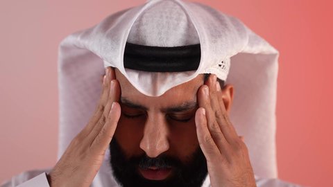 التعرض لنوبات الشقيقة الحادة، آلام الصداع النصفي، شاب سعودي يشعر بالحاجة لتناول المسكنات وأخذ قسط من الراحة، التعرض للتعب والإرهاق والعمل الطويل، بورتريه لرجل عربي خليجي قطري يرتدي الثوب التقليدي والغتره يمسك رأسه بيديه بإيماءات الألم، خلفية ملونة