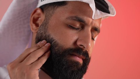 Problems of gingivitis and tooth decay, a young Saudi man feeling tired and exhausted, a close-up portrait of a Qatari Gulf Arab man wearing a traditional thobe and ghutra, putting his hand over his mouth with gestures of discomfort and severe pain, colored background