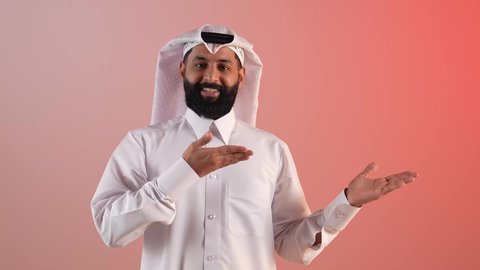 Gestures of pleasure and happiness, locating something, a young Saudi man pointing at someone, portrait of a smiling Qatari Gulf Arab man wearing a traditional thobe and ghutra pointing to the side, the concept of elegance and interest in one's appearance, colored background