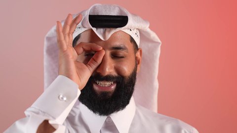 الاشارة بعلامة الامتياز، محاولة تقريب الأشياء البعيدة، حب الاكتشاف والمعرفة والمغامرة، التركيز على شيء ما، بورتريه مقرب لرجل عربي خليجي قطري يرتدي الثوب التقليدي والغترة، شاب سعودي يضع يده على عينه بشكل عدسة بإيماءات البحث، خلفية ملونة