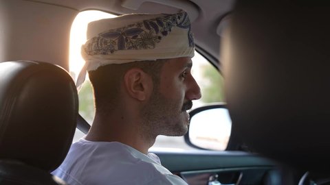 الالتزام بوضع حزام الأمان, مفهوم القيادة الآمنة, سائق عربي خليجي عماني يرتدي الدشداشة و العمامة يمسك المقود بيده و يقود السيارة بتعابير السعادة والسرور, خدمة النقل و التوصيل في سلطنة عمان