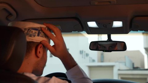 خدمة النقل و التوصيل في سلطنة عمان، الالتزام بوضع حزام الأمان, مفهوم القيادة الآمنة, سائق عربي خليجي عماني يرتدي الدشداشة ينظر الى المرآة ويقوم بتعديل العمامة، قيادة السيارة بتعابير السعادة والسرور