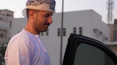 الاستعداد لركوب السيارة، مفهوم القيادة الآمنة, رجل عربي خليجي عماني يرتدي الدشداشة و العمامة يفتح باب السيارة الامامي، تعابير السعادة والسرور, خدمة النقل و التوصيل في سلطنة عمان