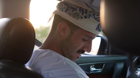 خدمة النقل و التوصيل في سلطنة عمان، الالتزام بوضع حزام الأمان, مفهوم القيادة الآمنة, سائق عربي خليجي عماني يرتدي الدشداشة و العمامة يمسك المقود بيده و يقود السيارة بتعابير السعادة والسرور