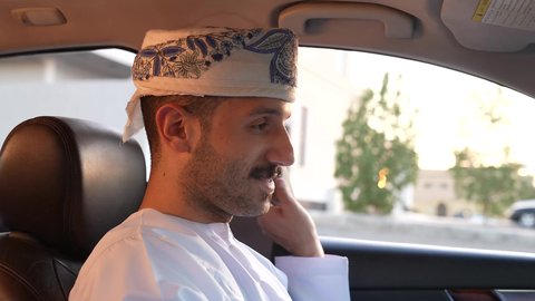 الالتزام بوضع حزام الأمان, مفهوم القيادة الآمنة, سائق عربي خليجي عماني يرتدي الدشداشة و العمامة يمسك المقود بيده و يقود السيارة بتعابير السعادة والسرور, خدمة النقل و التوصيل في سلطنة عمان