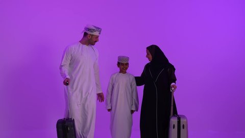 مفهوم السياحة والسفر، قضاء أوقات ممتعة في الإجازة, عائلة عربية خليجية عمانية تستعد للذهاب، المشي وجر حقائب السفر, تعابير السعادة والسرور, الاستعداد لوقت الرحلة، خلفية بنفسجية
