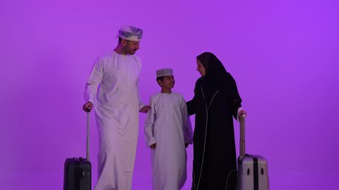مفهوم السياحة والسفر، قضاء أوقات ممتعة في الإجازة, عائلة عربية خليجية عمانية تستعد للذهاب، المشي وجر حقائب السفر, تعابير السعادة والسرور, الاستعداد لوقت الرحلة، خلفية بنفسجية