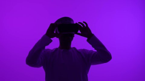 التطور التقني والتكنولوجي, المتعة و التسلية بالمشاهدة عبر نظارة الواقع الافتراضي، تصوير ظلي مقرب لشاب عربي خليجي عماني يرتدي الدشداشه والعمامة يضع نظارات ثلاثية الأبعاد (الفي ار), الاندماج ومحاكاة العالم الخيالي والنظر الى الافلام الواقعيه، خلفيه بنفسجية، سالوييت
