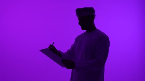تدوين وتسجيل الملاحظات والبيانات، تصوير ظلي مقرب لرجل عربي  خليجي عماني يرتدي الدشداشة والعمامة يقوم بالكتابة على الورق، خلفية بنفسجية، سالوييت