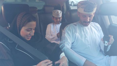 القيام بجولة ترفيهية بايماءات السرور، قضاء وقت ممتع مع الاسرة، ارتداء حزام الامان، رحله جماعيه عائليه في السياره، التنزه في شوارع سلطنه عمان مع العائلة، دردشه ومحادثات في الطريق، رجل عربي خليجي عماني يرتدي الدشداشة والعمامة يجلس مع زوجته وابنه داخل السياره