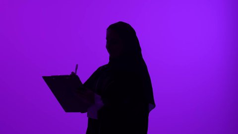 تدوين وتسجيل الملاحظات والبيانات، تصوير ظلي مقرب لامرأة عربية  خليجية عمانية ترتدي العباءة والحجاب تقوم بالكتابة على الورق، شابة سعودية تكتب المعلومات،  خلفية بنفسجية، سالوييت
