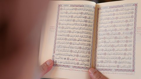 Reciting and reading the Holy Quran and contemplating its meanings, a close-up of an Arab Gulf Omani man wearing a dishdasha and turban holding the Holy Quran, frequently mentioning God Almighty, feeling reverence and tranquility, beige background
