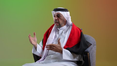 تشجيع الفريق المفضل، السرور لفوز المنتخب الوطني، إيماءات السعادة والفرح، رجل عربي خليجي كويتي يرتدي الثوب التقليدي يجلس على كرسي مريح يضع علم الكويت على كتفيه ، الشغف بمتابعة مباريات كرة القدم