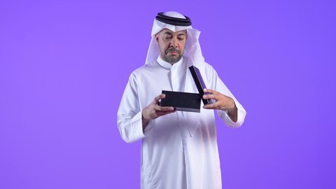 إيماءات السعادة والدهشة بالحصول على هدية ثمينة، فن انتقاء الهدايا بعناية، رجل عربي خليجي كويتي يرتدي الثوب التقليدي والغترة يقوم بفتح العلبة بتعابير الصدمة، رجل سعودي يقف بتعابير المفاجأة والإهداء