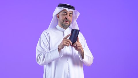 تصفح مواقع وتطبيقات الانترنت، النظر إلى الهاتف المحمول بإيماءات الاندماج، الدردشة والتحدث مع الأصدقاء، رجل عربي خليجي كويتي مبتسم يرتدي الثوب التقليدي والغتره يمسك الجوال بيده، رجل سعودي يستخدم التقنيات والتكنولوجيا الحديثة بالحياة اليومية