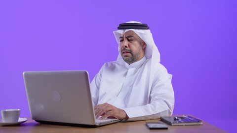 التركيز والتفاني والعمل الجاد، التوظيف في المكاتب والشركات الكويتية، رجل عربي خليجي كويتي يرتدي الثوب التقليدي والغترة يجلس على مكتب ويعمل على جهاز الحاسب المحمول ،موظف سعودي يستخدم التقنيات الحديثة في الأعمال الإدارية والمكتبية