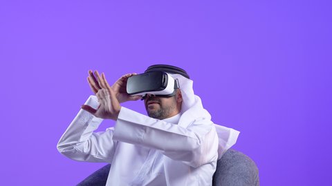 المتعة والتسلية بالمشاهدة عبر نظارة الواقع الافتراضي, رجل عربي خليجي كويتي يرتدي الثوب التقليدي والغترة يجلس على كرسي يضع نظارات ثلاثية الأبعاد يقوم برفع كف يده للاعلى بتعابير الاندماج ,  رجل سعودي يشير بايماءات التوقف عن فعل امر ما