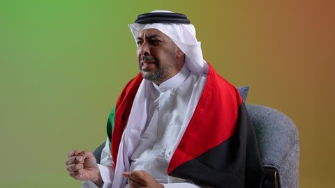 السرور لفوز المنتخب الوطني، إيماءات السعادة والفرح، رجل عربي خليجي كويتي يرتدي الثوب التقليدي يجلس على كرسي مريح يضع علم الكويت على كتفيه ، تشجيع الفريق المفضل، الشغف بمتابعة مباريات كرة القدم