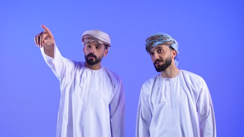 اشارات تحديد هذا المكان (هنا)،  النظر إلى الأعلى بإيماءات التعجب و الاندهاش, بورترية لرجلان عربيان خليجيان عمانيان يرتديان الدشداشة و العمامه يشيران بإصبع السبابة الى الاعلى, خلفية زرقاء
