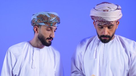 الاستمتاع بممارسة هواية المطالعة, قضاء وقت الفراغ بالتعلم والثقافة، القراءة بتمعن وتركيز، بورتريه لرجل عربي خليجي عماني يرتدي الدشداشة و العمامه يحمل بيده كتاب تثقيفي برفقه صديقة